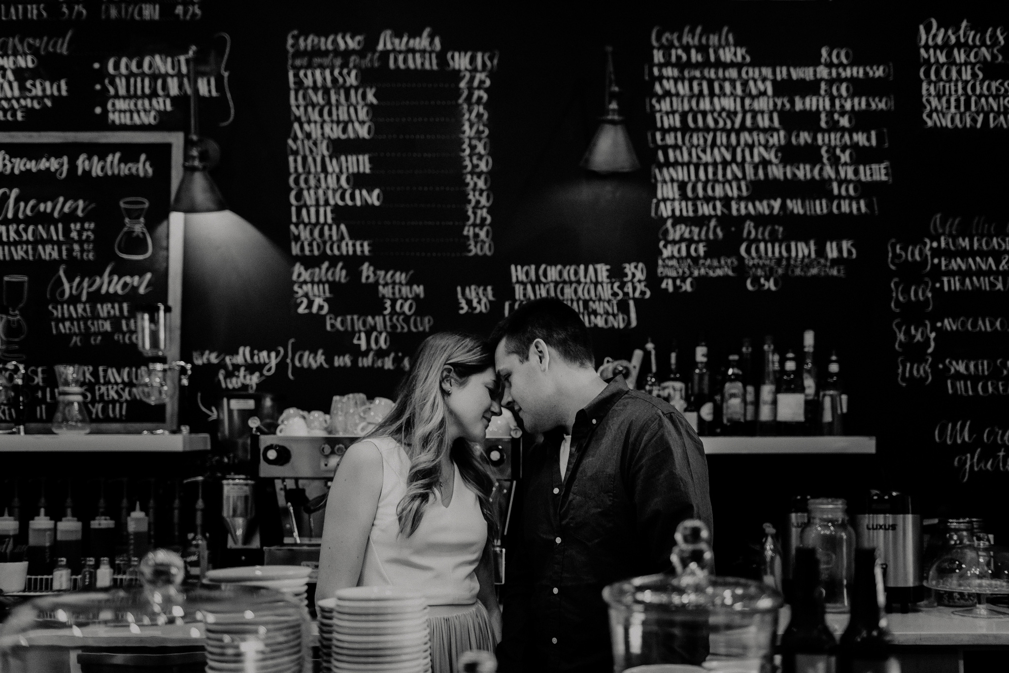 indie couple touching foreheads behind counter of cafe
