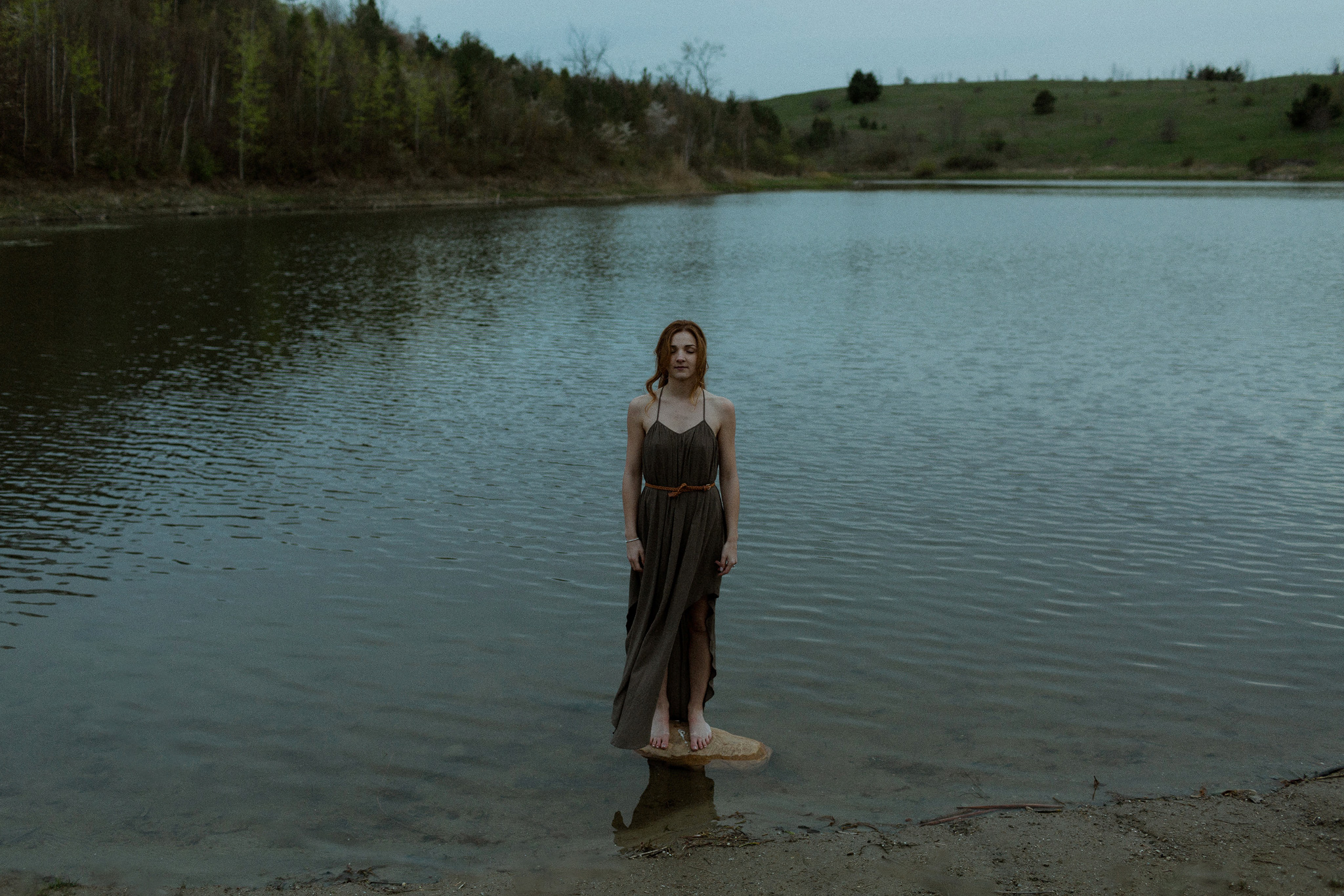 portrait of girl in dress standing on a rock in the middle of kettle lake in forks of the credit