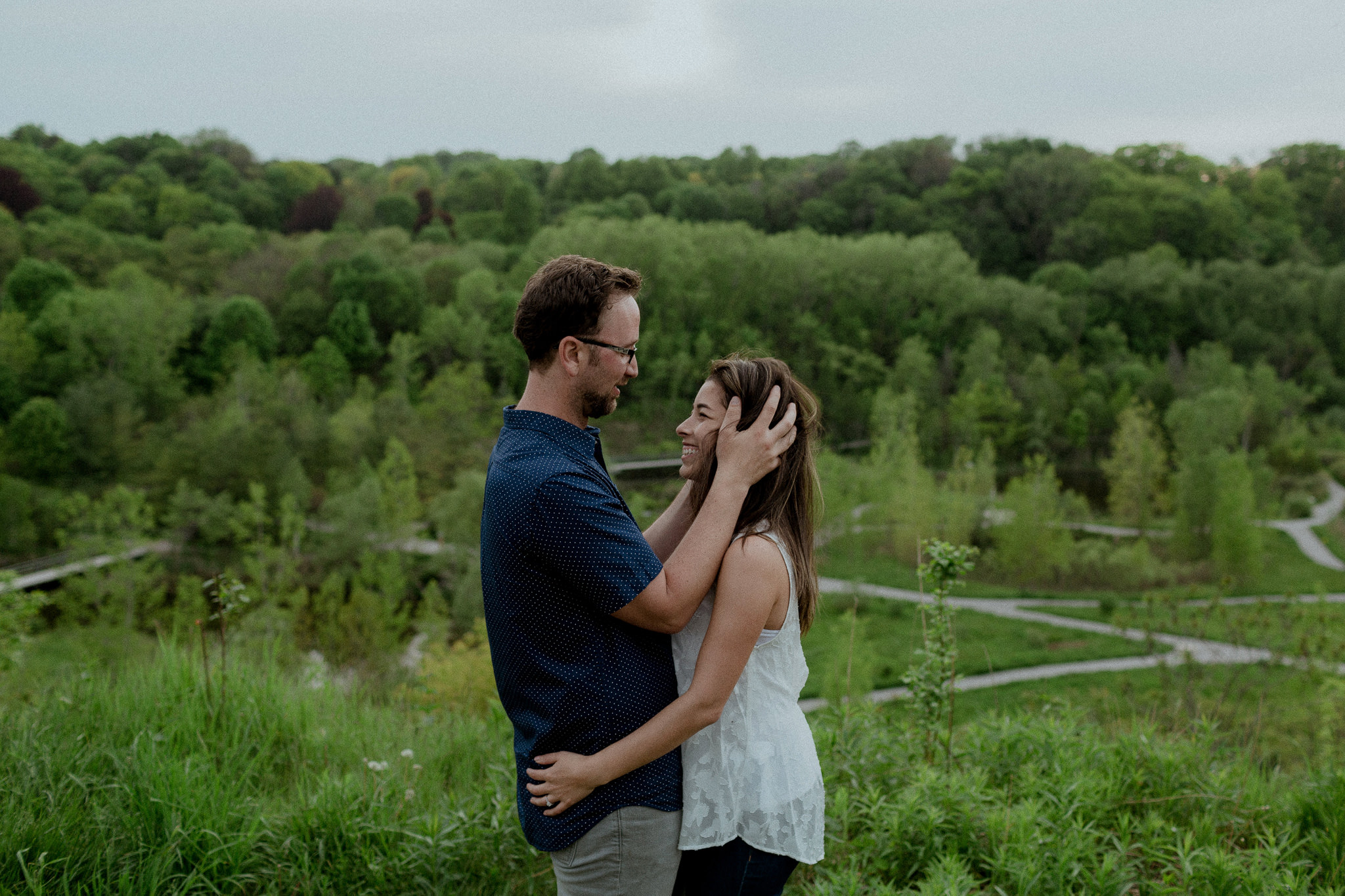 Couple holding each other with Toronto fields and forest in distance 