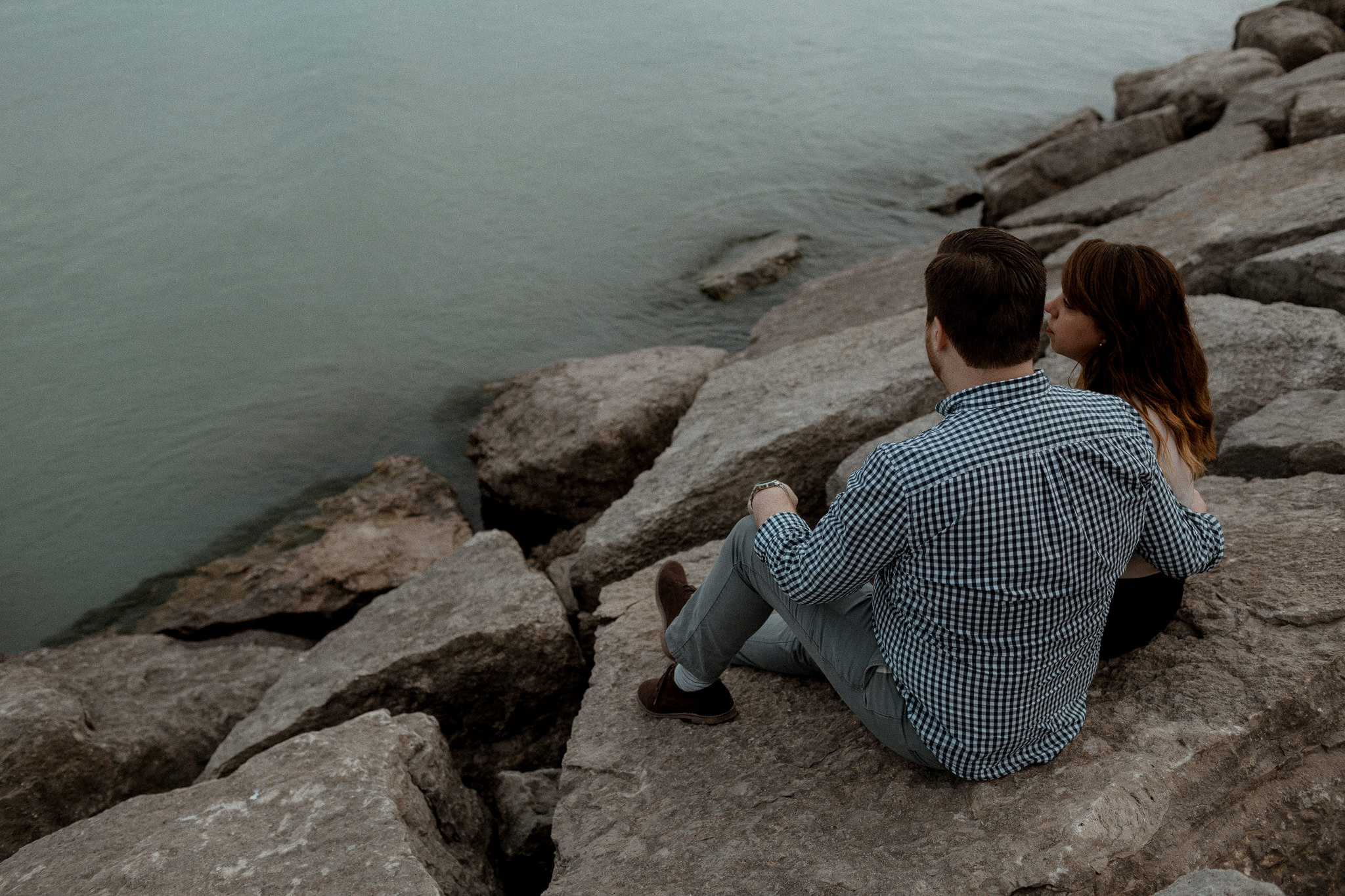 Engaged couple sitting on rocks by the water in Scarborough 